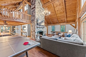 A spacious living area with a ping pong table, a stone fireplace, and a cozy seating area.
