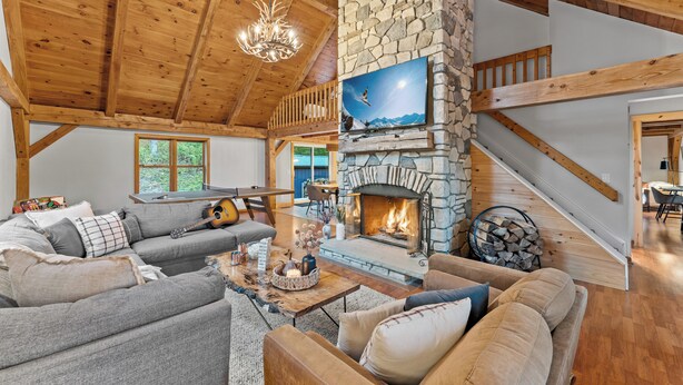 A cozy living room with a stone fireplace, wooden beams, and a comfortable seating area. - Beautiful chalet on 5 acres - 2 min to Village!👌 Hot-Tub, Sauna, Fire Pit🔥 (Ellicottville)