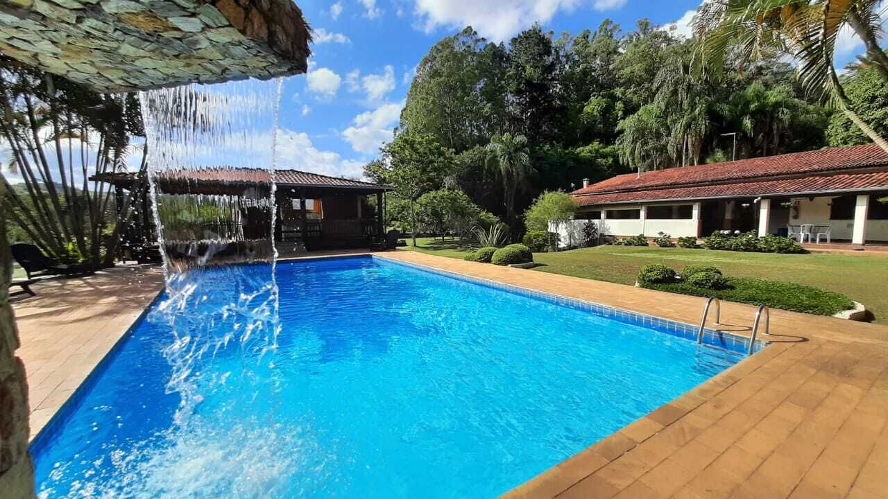 A swimming pool with a waterfall feature, surrounded by a wooden deck and lush greenery.