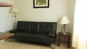 A living room with a black leather sofa, two floor lamps, a small wooden side table, and a framed picture on the wall. - Villa Centro Casa Divina (Oaxaca)