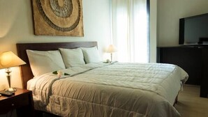 A neatly made bed with a white comforter and pillows, a bedside table with a lamp, a wall-mounted TV, and a decorative piece above the bed. - Villa Centro Casa Divina (Oaxaca)