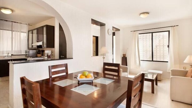 A modern kitchen with dark cabinets, a dining table with chairs, and a fruit bowl. - Villa Centro Casa Divina (Oaxaca)