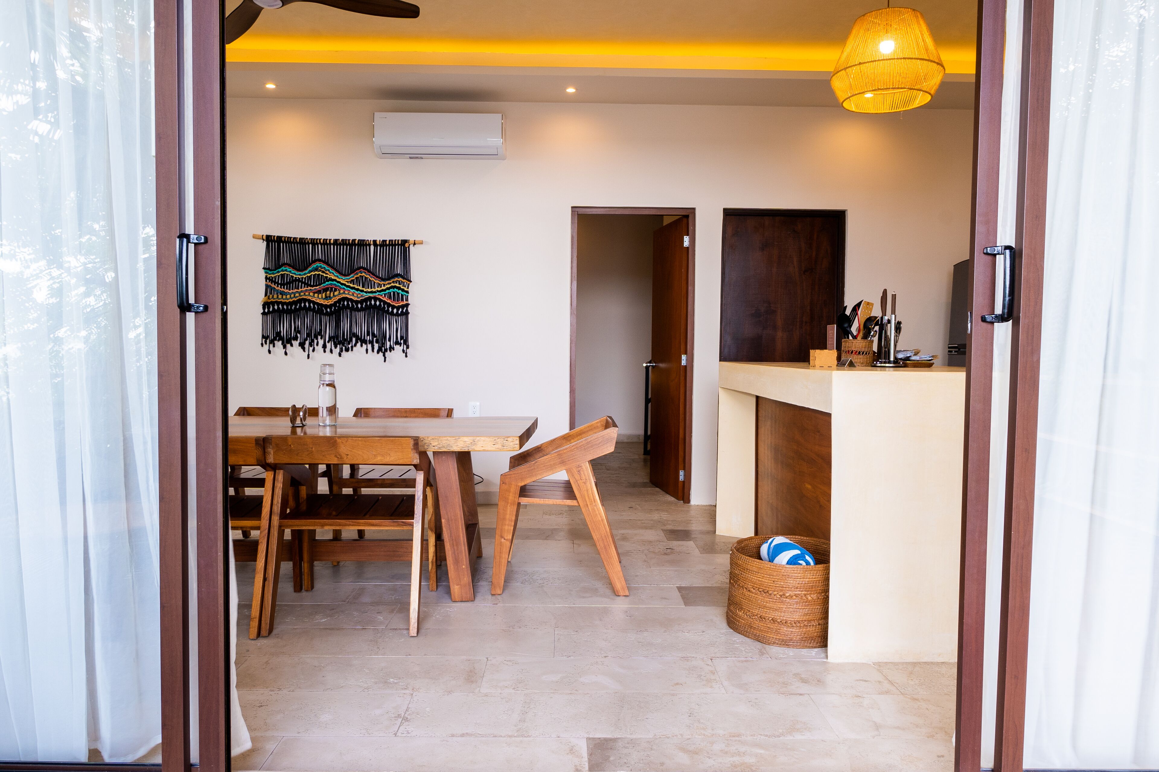 A dining area with a wooden table and chairs, a woven wall hanging, and a basket with items.