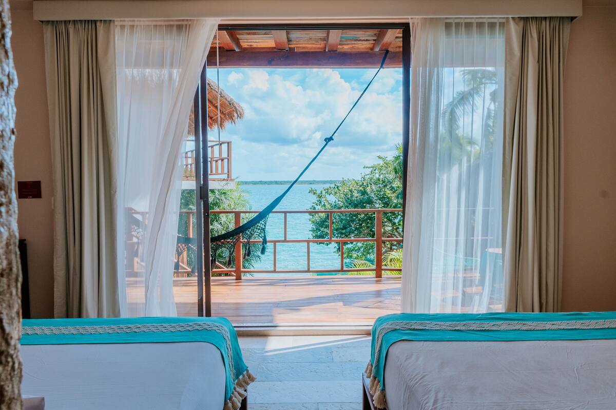 A room with two beds, a view of the sea, and a hammock.