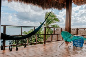 A hammock and chairs on a wooden deck with a view of the sea and palm trees. - Khaban Bacalar Hotel Boutique (Bacalar)