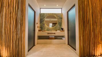 Bathroom features a central vanity with sink, countertop, and storage, alongside a large mirror and vertical wall slats.