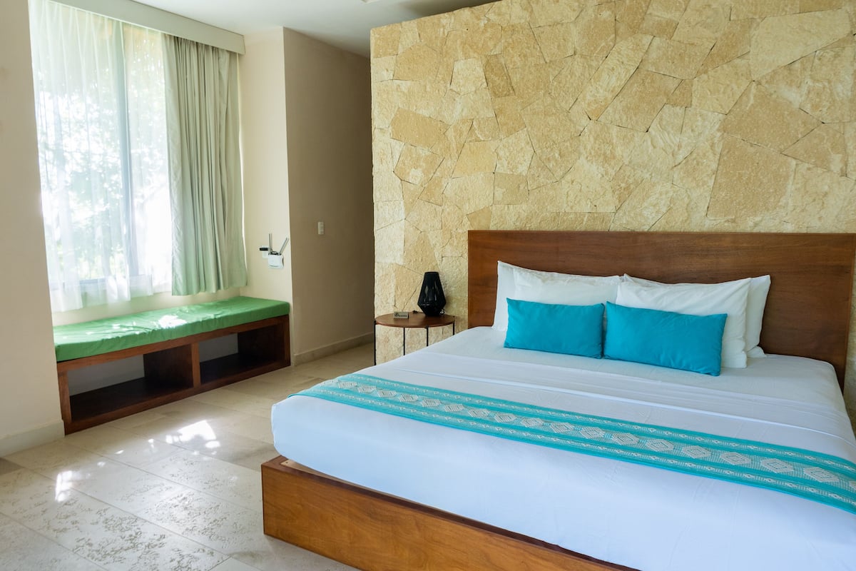 A hotel room with a large bed, a bench at the window, and a stone wall.