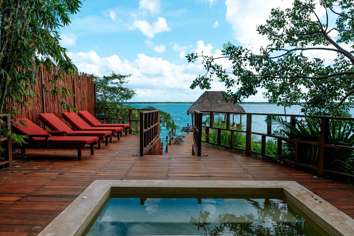 A wooden deck with red lounge chairs, a pool, and a view of the sea.