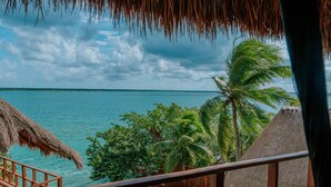 A wooden deck with a thatched roof overlooking a turquoise sea and palm trees. - Khaban Bacalar Hotel Boutique (Bacalar)