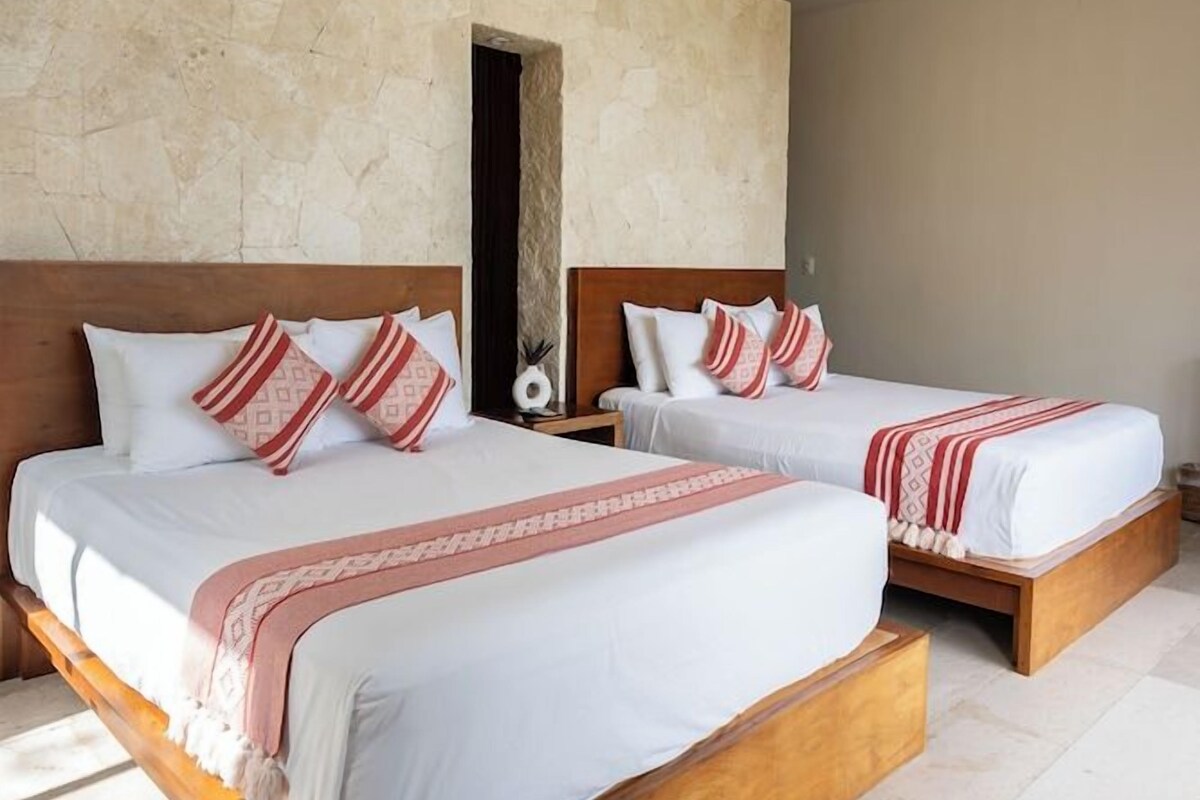 A hotel room with two wooden beds, a ceiling fan, and a stone wall.