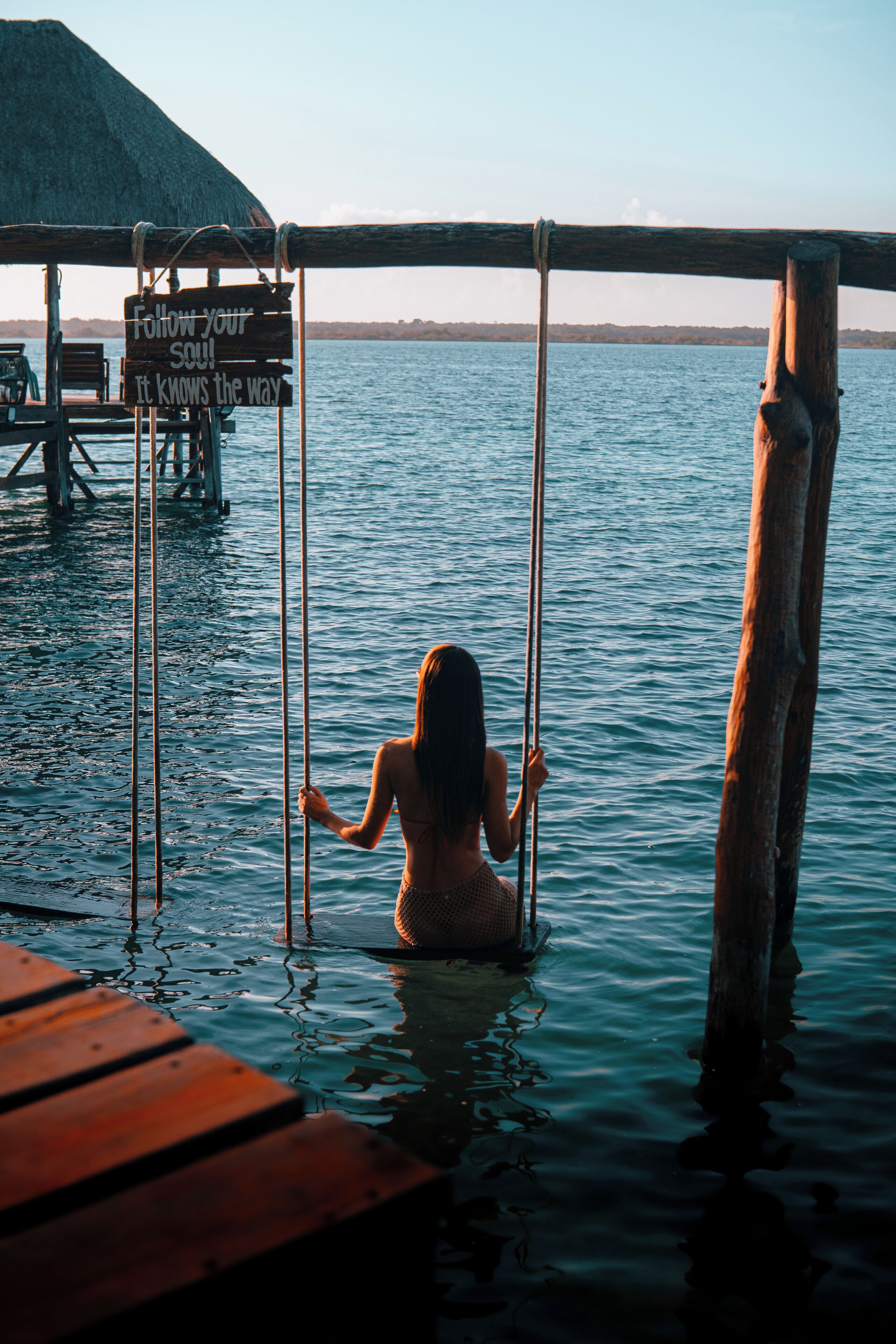 A wooden dock extending into calm water with a person sitting on a swing.