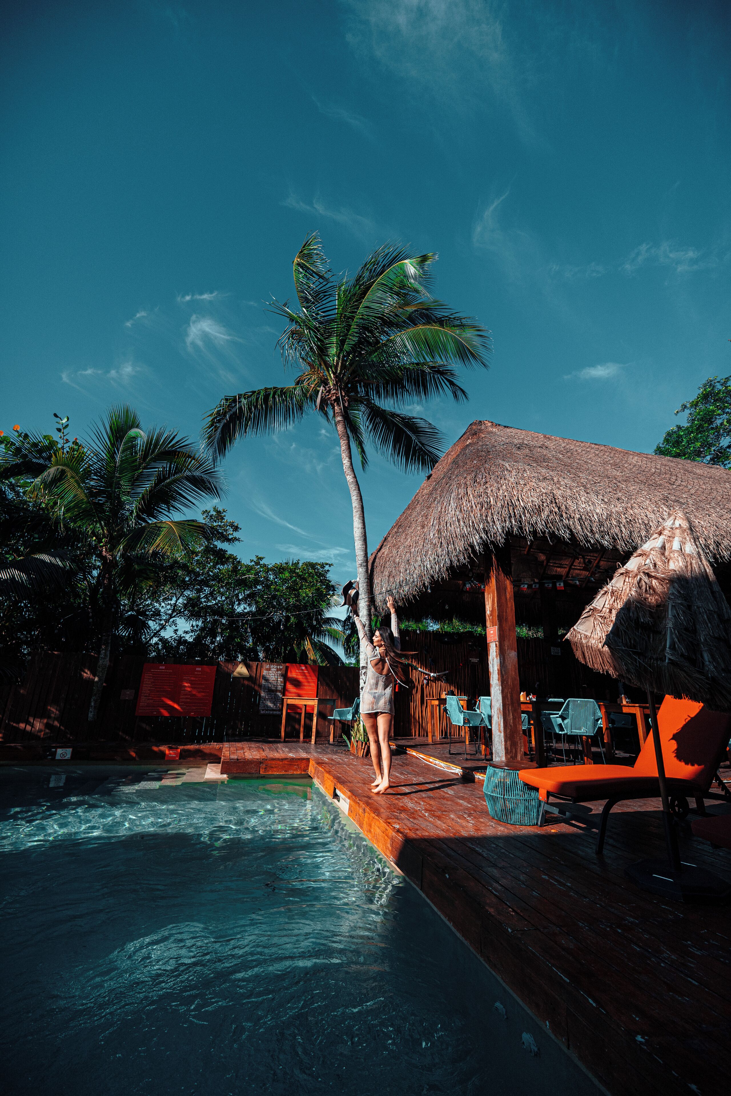A pool area with a thatched-roof structure, wooden deck, and lounge chairs.