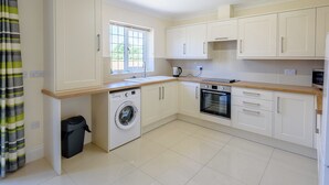 A modern kitchen with white cabinets, a built-in washing machine, an oven, and a window with a view of greenery outside. - Dawson Park 5 - UK12664 (Mablethorpe)