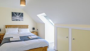 A bedroom with a wooden bed, a nightstand, a lamp, a framed picture on the wall, and a wardrobe. - Dawson Park 5 - UK12664 (Mablethorpe)