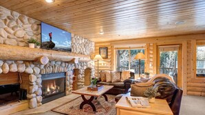 A log cabin interior with a stone fireplace, a leather sofa, and a television mounted on the wall.