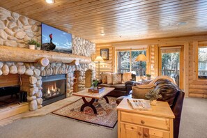 A log cabin interior with a stone fireplace, a leather sofa, and a television mounted on the wall.