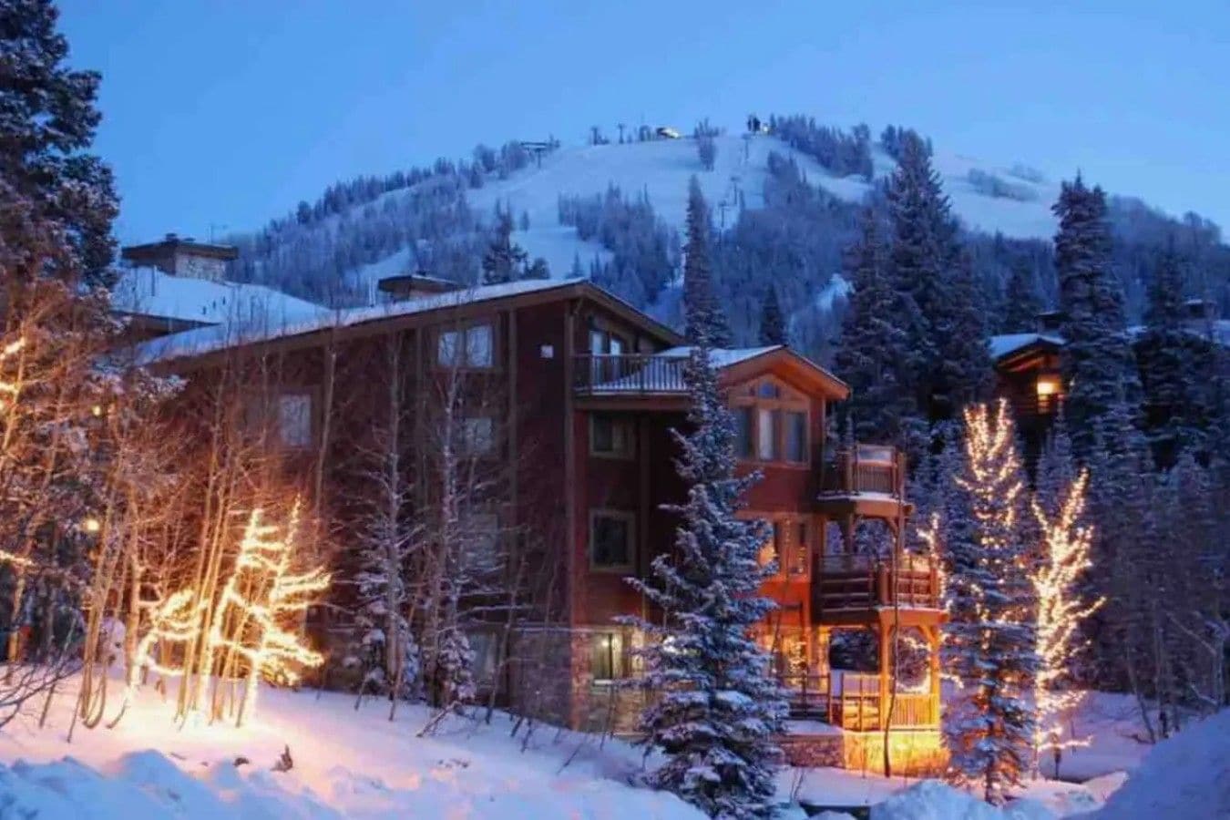 A lodge with multiple floors, surrounded by snow-covered trees and a mountain backdrop.