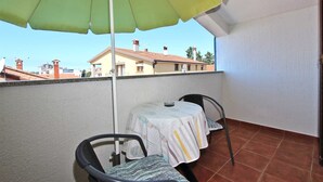 En balkon med et bord og stole, en grøn parasol og udsigt til bygninger i baggrunden.