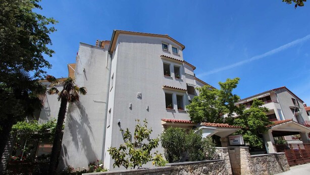 A multi-story residential building with a stone wall in front, several balconies, and a clear blue sky.