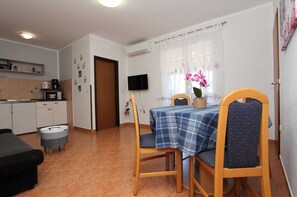 A dining area with a table set for two, a television mounted on the wall, and a kitchen in the background.