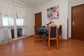 A dining area with a table set for four, chairs, a floral painting on the wall, and a sliding glass door with curtains.