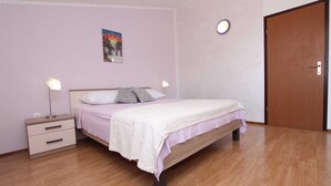 A bedroom with a bed, bedside tables, a nightstand, a door, and a wall-mounted light fixture.