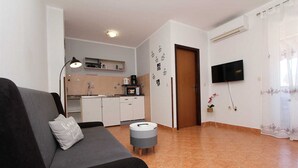 A living room with a sofa, a small table, a TV, and a kitchen in the background.