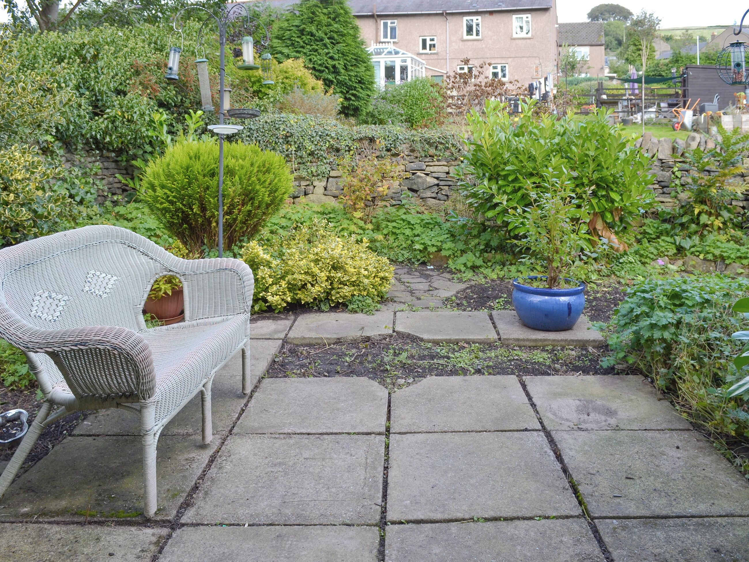 A garden patio with a wicker chair, a potted plant, and a stone pathway.