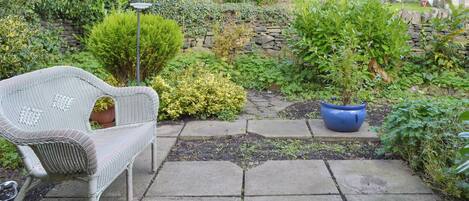 A garden patio with a wicker chair, a potted plant, and a stone pathway.