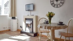 Un comedor con una mesa redonda, sillas, un reloj, una chimenea y un televisor montado en la pared.