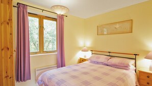 Una camera da letto con un letto, un comodino, una lampada, una finestra con tende e una sveglia a parete.