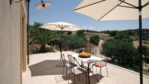 An outdoor patio with a table, chairs, and umbrellas. - Nice apartment with private terrace. Shared pool. In Donnafugata, Sicily (Donnafugata)