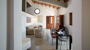 A spacious living area with a dining table, chairs, and a sofa. There is a wooden ceiling and a round window. - Nice apartment with private terrace. Shared pool. In Donnafugata, Sicily (Donnafugata)