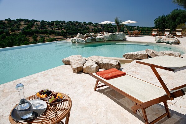 A poolside area with lounge chairs, a fruit basket, and a bottle of water.