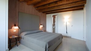 A bedroom with a large bed, wooden ceiling beams, two bedside lamps, and a door leading to a bathroom. - Nice apartment with private terrace. Shared pool. In Donnafugata, Sicily (Donnafugata)