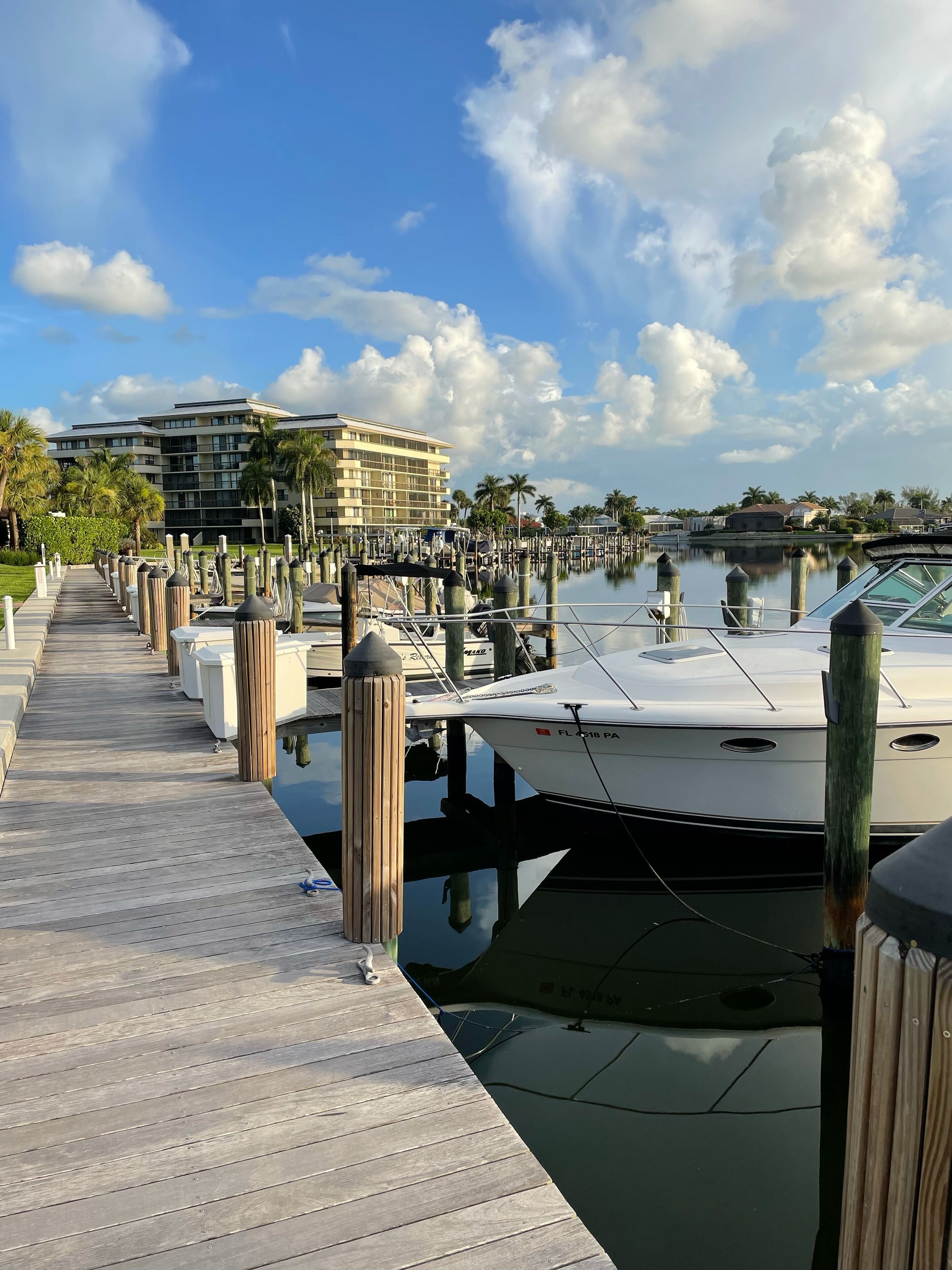 A marina with boats docked, a wooden walkway, and a building in the background.