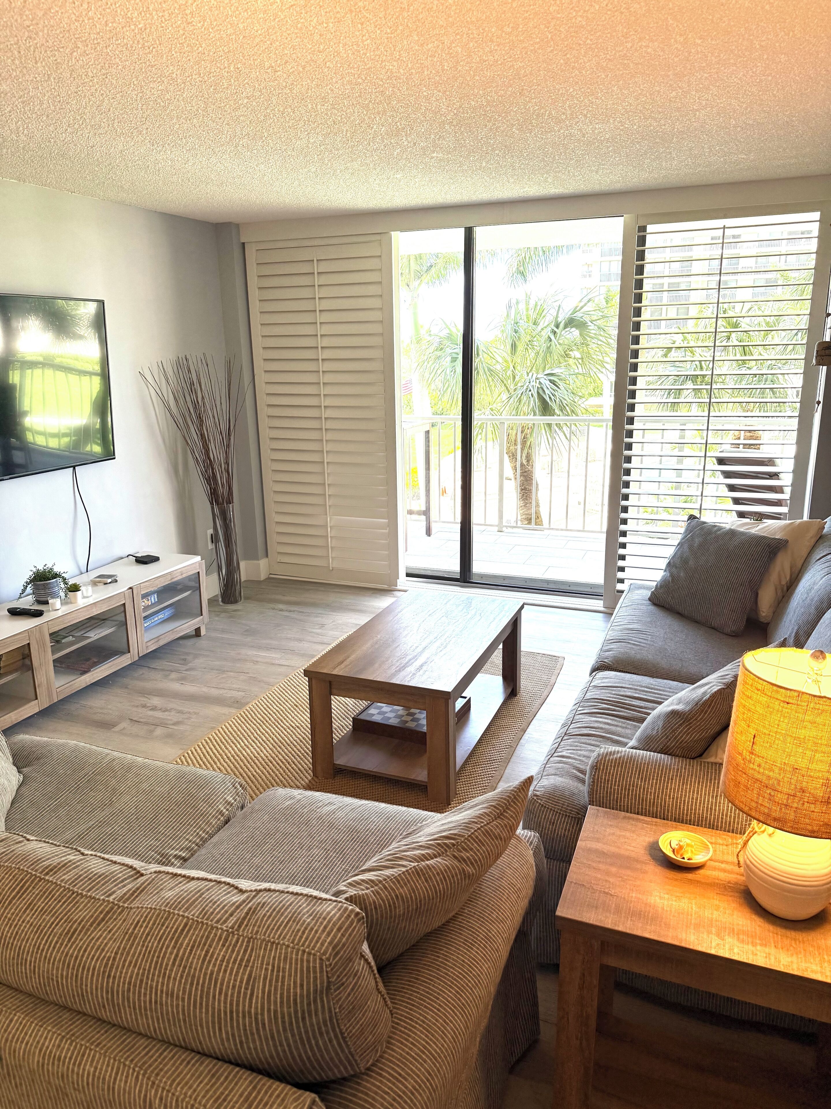 A living room with a sofa, a coffee table, a TV, and a sliding glass door leading to a balcony.