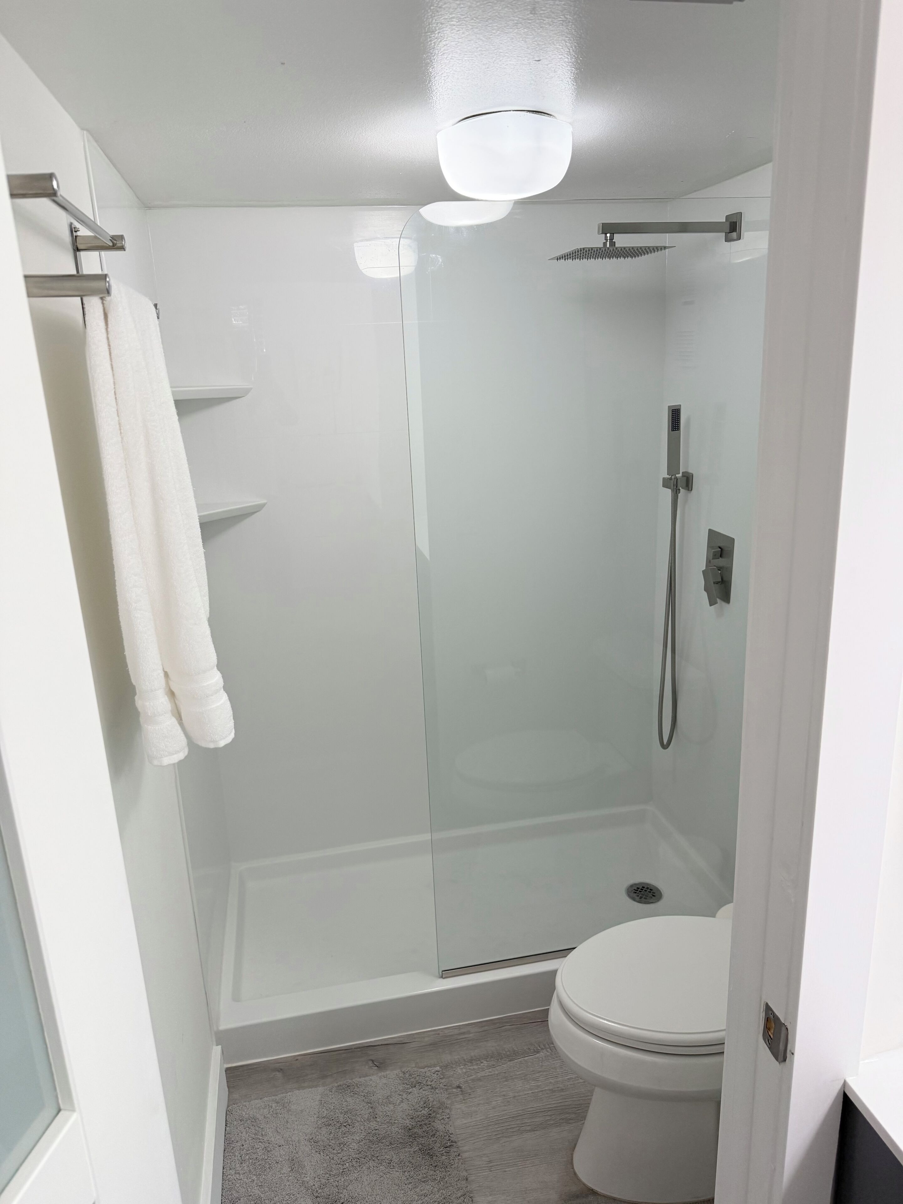 A modern bathroom with a glass-enclosed shower, a toilet, and a towel rack.