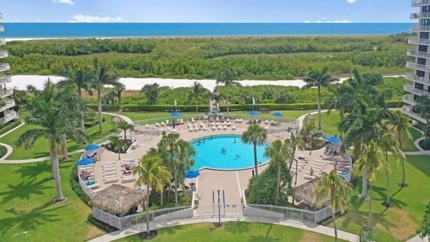 A resort pool with a view of the ocean, surrounded by palm trees and lounge areas. - Beach Front Condo in Paradise Marco Island (Marco Island)