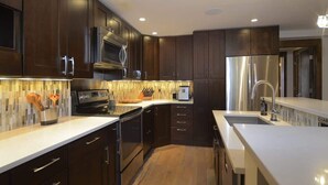 Une cuisine moderne avec des meubles en bois foncé, des appareils électroménagers en acier inoxydable et un plan de travail blanc.