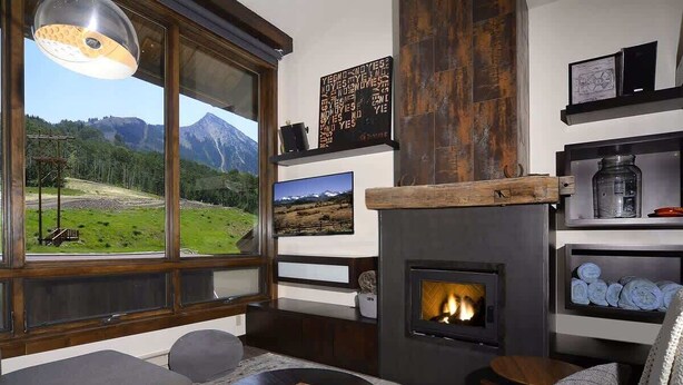 Un salon moderne doté d’une cheminée, de grandes fenêtres offrant une vue sur les montagnes et d’un coin salon confortable.