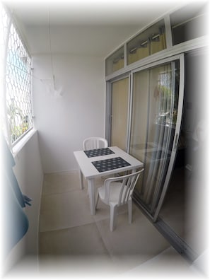A small balcony with a white table and two chairs, a window with a metal grill, and a sliding glass door. - Studio Terrace sea view (Les Trois-Îlets)