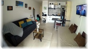 A living room with a sofa, coffee table, and a TV. There is a kitchen area with cabinets, a microwave, and a refrigerator. - Studio Terrace sea view (Les Trois-Îlets)