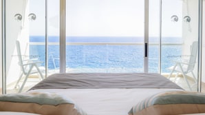 A bedroom with a large bed, two white chairs, and a view of the sea. - Perla Gris Aparthotel (Adeje)