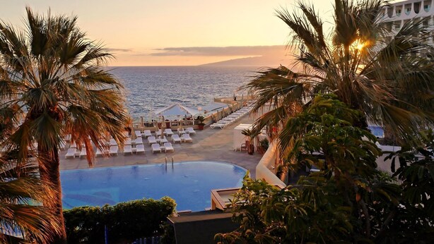 A poolside view with lounge chairs and palm trees, overlooking the sea. - Perla Gris Aparthotel (Adeje)