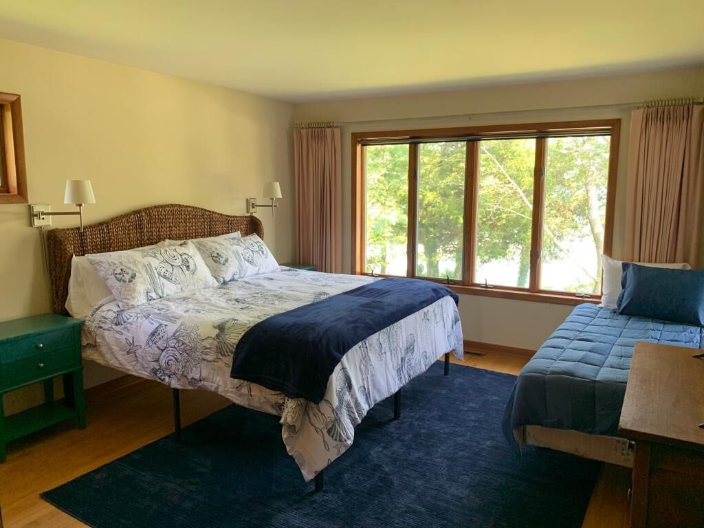 Ein Schlafzimmer mit einem großen Bett, einem Nachttisch, einem Stuhl und einem Fenster mit Vorhängen.