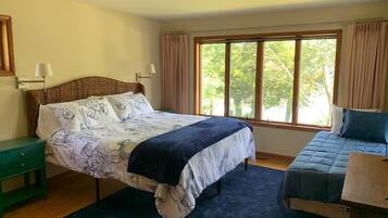 Ein Schlafzimmer mit einem großen Bett, einem Nachttisch, einem Stuhl und einem Fenster mit Vorhängen.