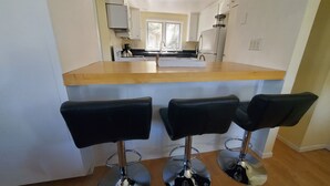 A kitchen with a wooden countertop, three black bar stools, and a view into the dining area. - Woodland Pines Cabin (Frazier Park)