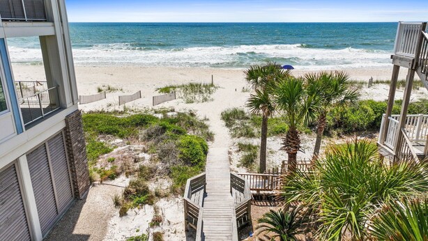 A beach view with a wooden pathway leading to the ocean, surrounded by palm trees and a wooden deck.