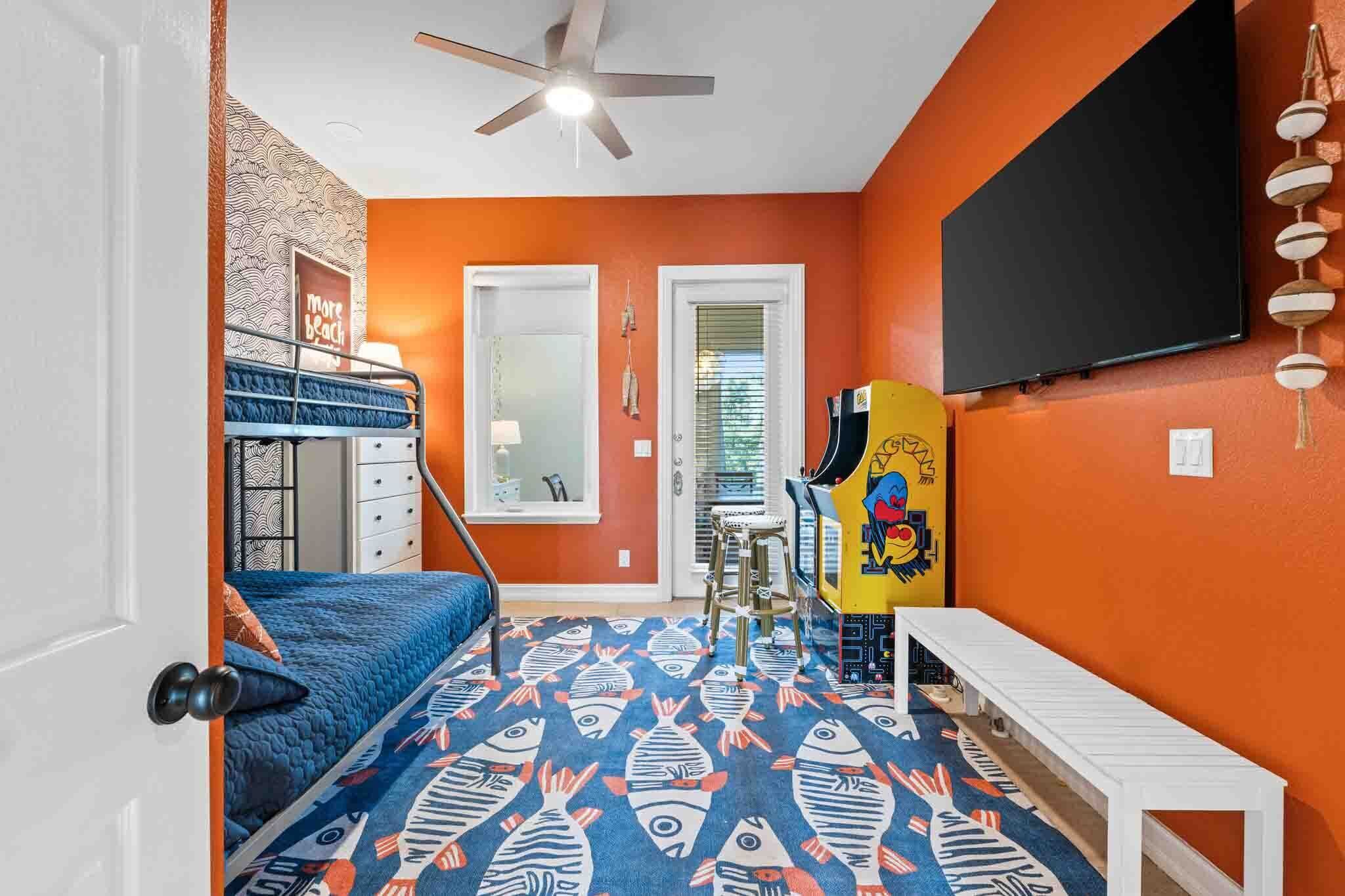 A room with a bunk bed, a ceiling fan, a TV, and a colorful fish-patterned rug.